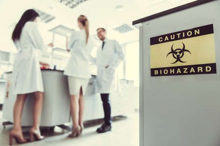 At the laboratory. Inscription "Caution Biohazard". Medical doctors are working in the backgroundの写真素材