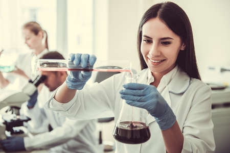 Beautiful medical doctor in gloves is smiling while working with test tubes at the labの写真素材