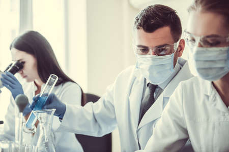 Beautiful medical doctors in gloves, masks and glasses are working with substances in test tubes and microscope at the labの写真素材