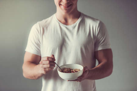 Handsome guy is smiling while holding a bowl with porridge, on gray backgroundの写真素材