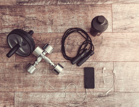 Top view of dumbbells, exercise wheel, jumping rope, shaker and smart phone with earphones - best...