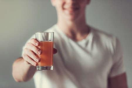 Cropped image of handsome guy holding a glass of orange juice, on gray backgroundの写真素材