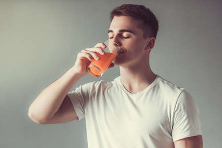 Handsome guy is drinking orange juice, on gray backgroundの写真素材