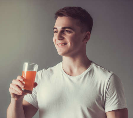 Handsome guy is smiling while holding a glass of orange juice, on gray backgroundの写真素材