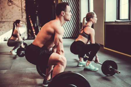 Beautiful young sports people are working out with barbells in gymの写真素材