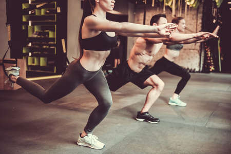 Beautiful young sports people are working out with TRX in gymの写真素材