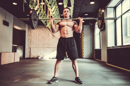 Handsome young muscular sportsman is working out with barbell in gym