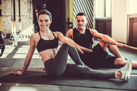 Beautiful young sports couple is stretching after workout in gym