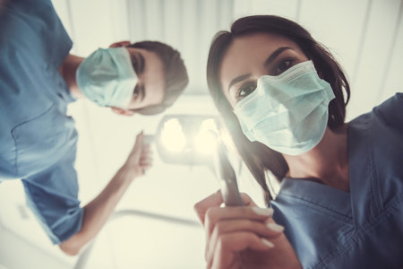 Bottom view of dentists in surgical mask holding tools and looking at cameraの写真素材