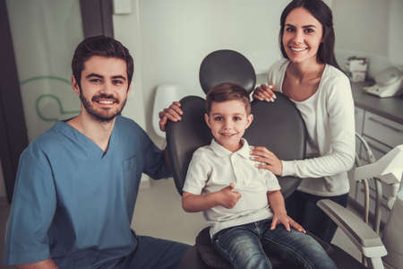 Cute little boy at the dentist. Mom, doctor and boy are looking at camera and smilingの写真素材