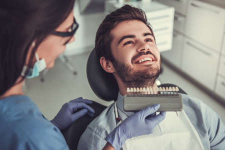Handsome young man is sitting in dentist's chair while doctor is examining his teethの写真素材