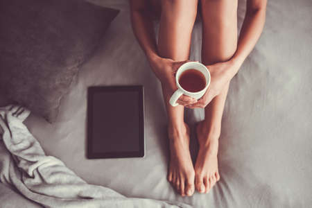 Good morning! Happy young beautiful woman drinks tea sitting on the bed. Top view.の写真素材