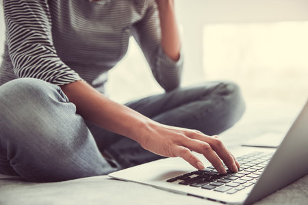 Home office. Woman sitting on bed, working on laptop.