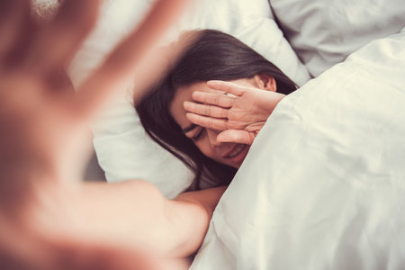Top view. Shy young beautiful girl hides his face, waking up in a bed in a bedroom at home