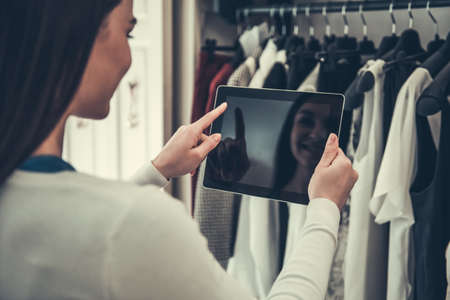 Back view of beautiful female shop assistant using a digital tablet and smiling while standing in boutiqueの写真素材
