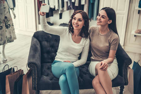 Beautiful girls are doing selfie using a smart phone and smiling while doing shopping in boutiqueの写真素材