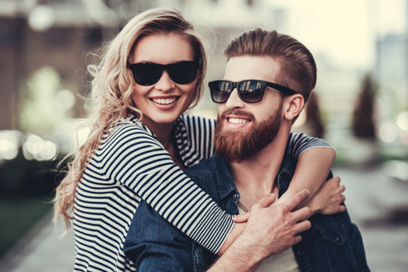 Beautiful young couple in sun glasses hugging, looking at camera and smiling while standing outdoors