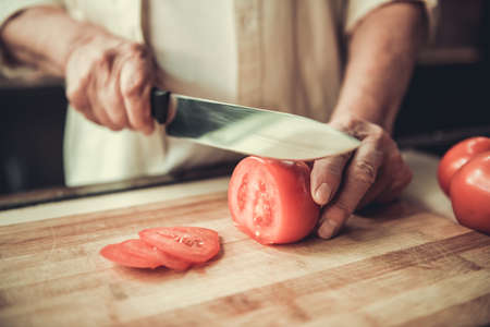 Cropped image of handsome senior man cutting tomato while cooking in kitchenの写真素材