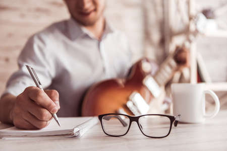 Handsome young businessman is playing guitar, making notes and smiling in his office during the break, croppedの写真素材