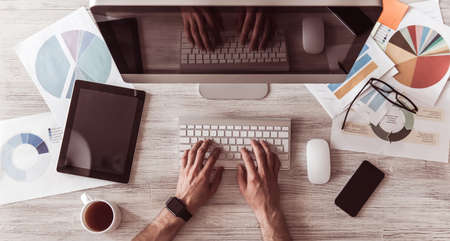 Top view of businessman's working place with computer, other gadgets and documents, man is typing, croppedの写真素材