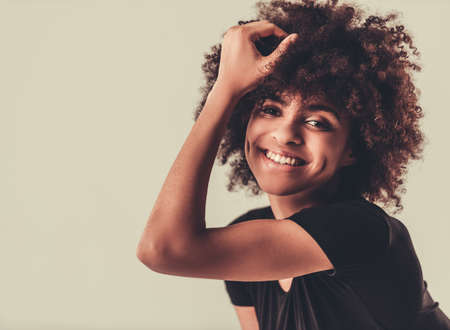 Portrait of beautiful Afro American girl looking at camera and smiling, on light backgroundの写真素材
