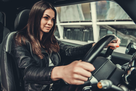 Beautiful girl in leather jacket is driving a car