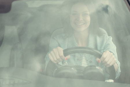 View through the windshield of beautiful girl smiling while driving a car