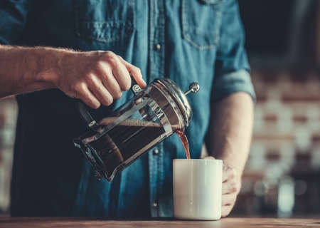 Cropped image of young man pouring coffee into the cup while standing in kitchenの写真素材