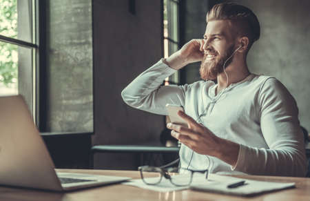 A young bearded man listening to music on headphones, sitting at his workplace in the officeの写真素材