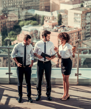 High angle view of beautiful business people discussing documents while standing on balcony of the office building during coffee breakの写真素材