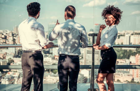 Beautiful business people are communicating on balcony of the office building during coffee break. Afro American lady looking at camera and smilingの写真素材