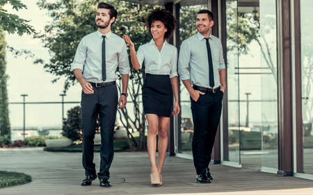 Full length portrait of beautiful business people smiling while walking outdoorsの写真素材