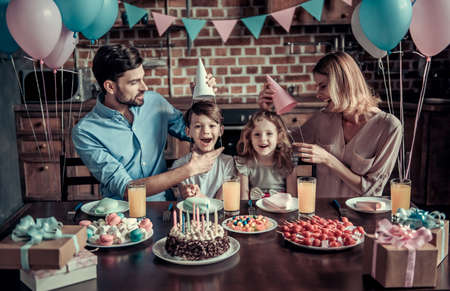 Happy family is smiling while sitting at the table in decorated kitchen during birthday celebration, kids are looking at cameraの写真素材