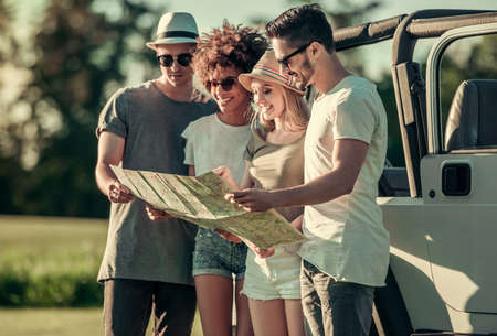 Happy young people are studying map and smiling while travelling by car in sunny weatherの写真素材