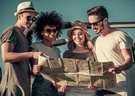Happy young people are studying map and smiling while travelling by car in sunny weather