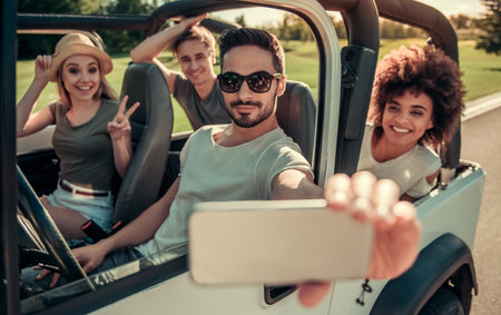Happy young people are taking photo using a smart phone and smiling while travelling by car in sunny...