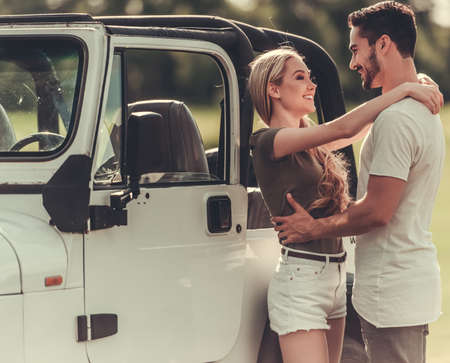 Young couple hugging, looking at each other and smiling while leaning on their car, outdoorsの写真素材