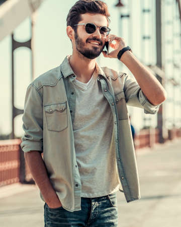 Handsome guy is talking on the mobile phone and smiling while walking outdoorsの写真素材