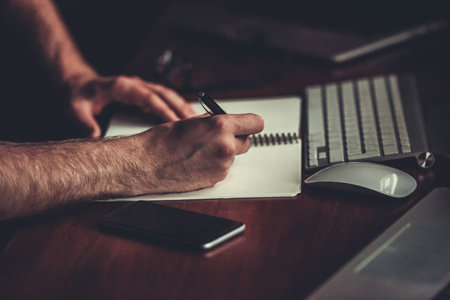 Cropped image of young businessman making notes while working with a computer at night
