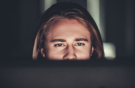 Handsome young businessman with shoulder-length blond hair is working with a computer at night
