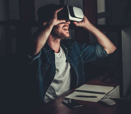 Handsome young man with shoulder-length blond hair is using with a virtual reality headset at nightの写真素材