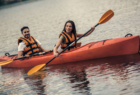 Happy young couple in sea vests is smiling while sailing a kayakの写真素材
