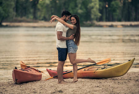 Happy young couple is hugging and smiling while standing near the kayaks on the beach after sailingの写真素材