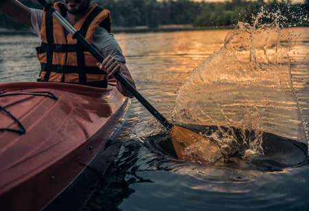 Cropped image of handsome young man in sea vest sailing a kayak