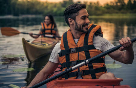 Happy young couple in sea vests is smiling while sailing kayaksの写真素材