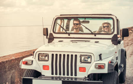 Beautiful young couple is smiling while travelling by car in sunny weatherの写真素材