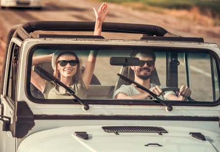 Beautiful young couple is smiling while travelling by car in sunny weather
