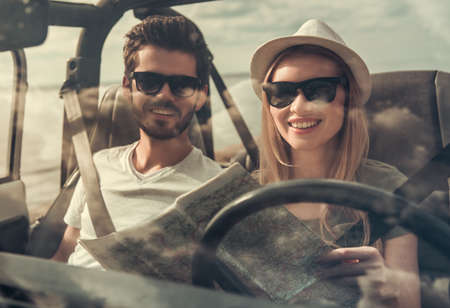 Beautiful young couple is studying map and smiling while travelling by carの写真素材