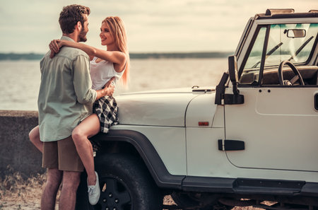 Beautiful couple is hugging and smiling while leaning on their car