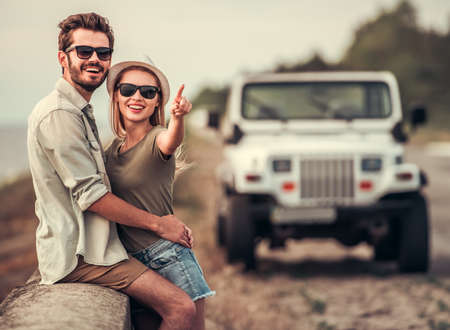 Beautiful couple is hugging and smiling while resting near the sea during their car tripの写真素材